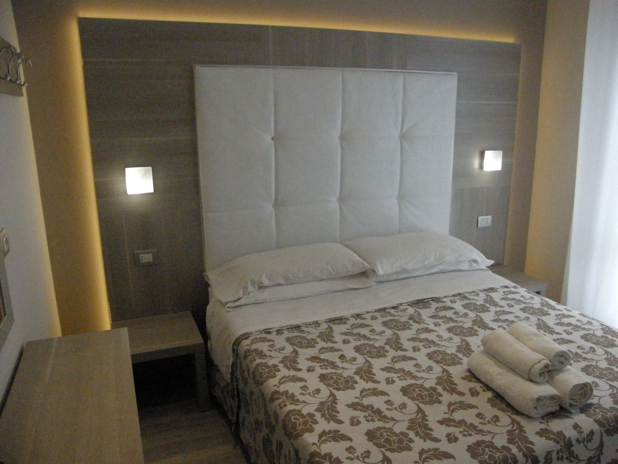 Een hotelkamer met een groot bed, een nachtkastje en een hoofdbord met ingebouwde verlichting.