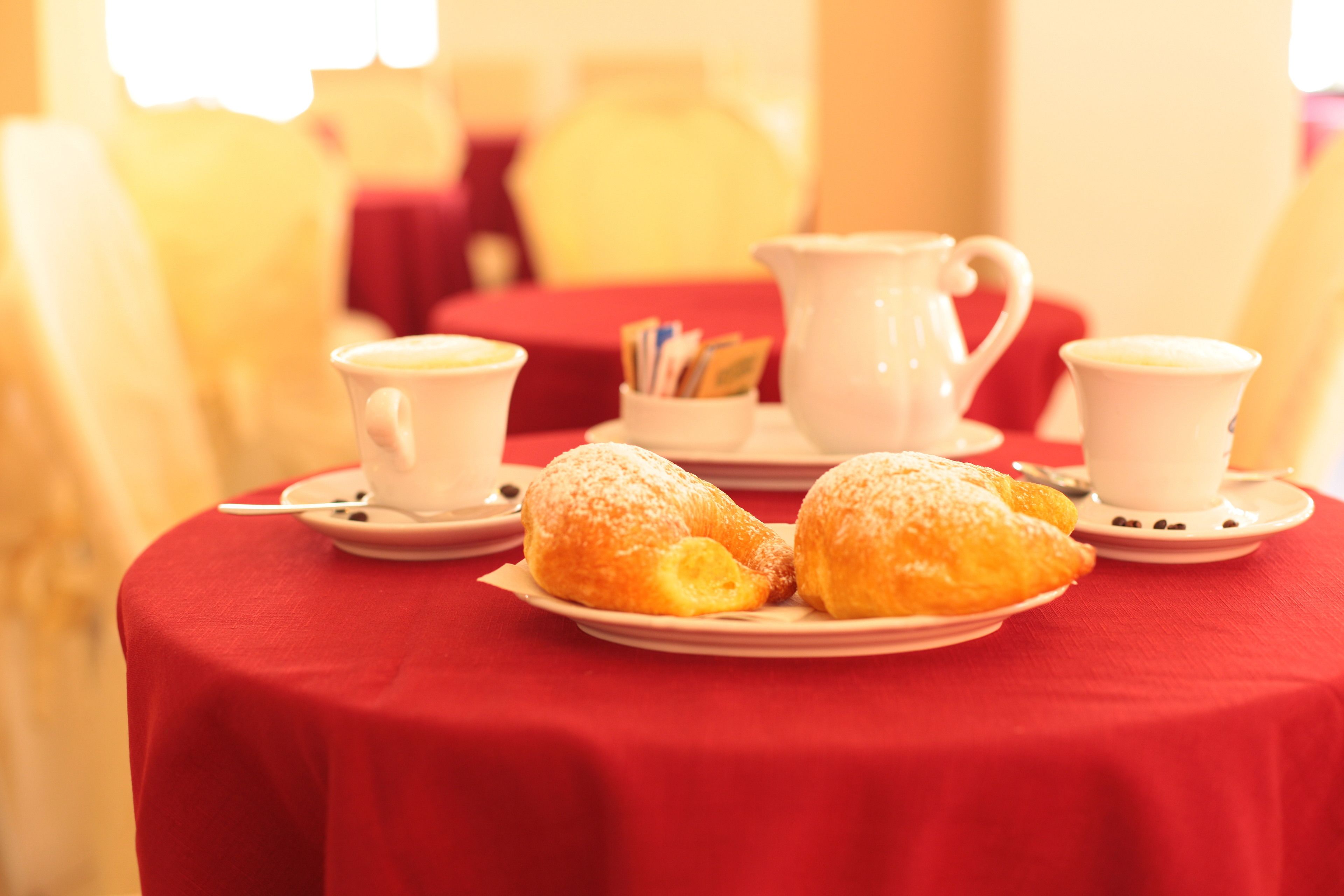 A table with pastries, a pitcher, and cups on a red tablecloth.