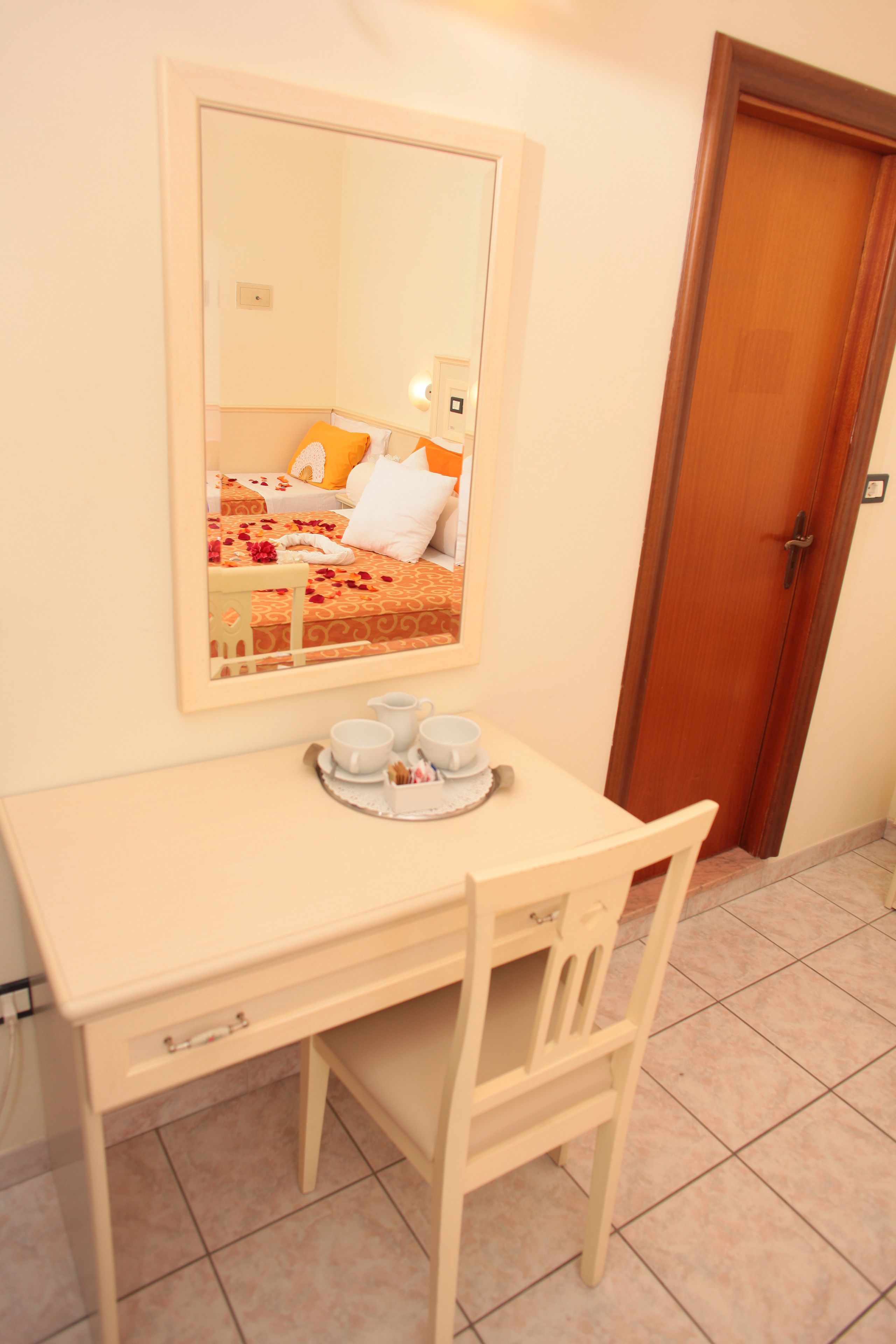 Una habitación pequeña y ordenada, con una cama, una mesita de noche con tazas y una bandeja, y un espejo en la pared.