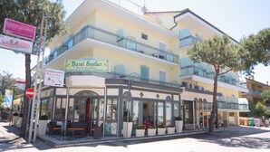 Un hotel de dos pisos con balcones, una cafetería y mesas al aire libre.