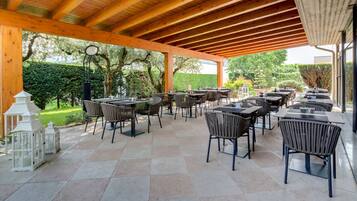Una terrazza esterna con diversi tavoli e sedie, circondata da una pergola in legno e vista su un giardino.