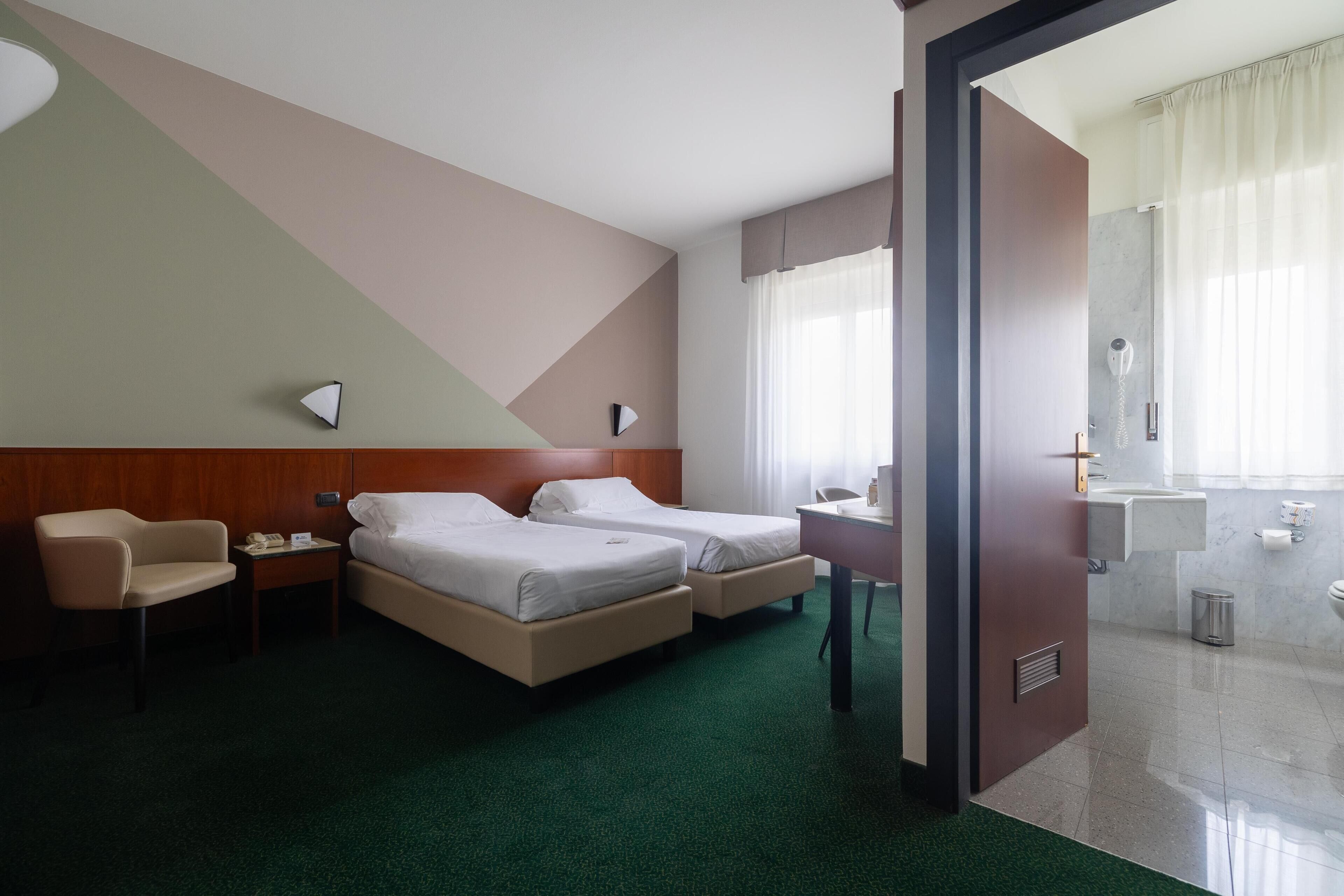 A hotel room with two beds, a desk, a chair, a phone, and a bathroom visible through an open door.