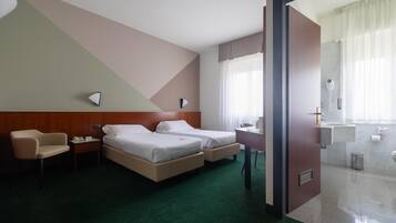 A hotel room with two beds, a desk, a chair, a phone, and a bathroom visible through an open door.