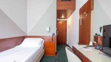 A hotel room with a bed, a desk with a computer, a telephone, and a mirror.