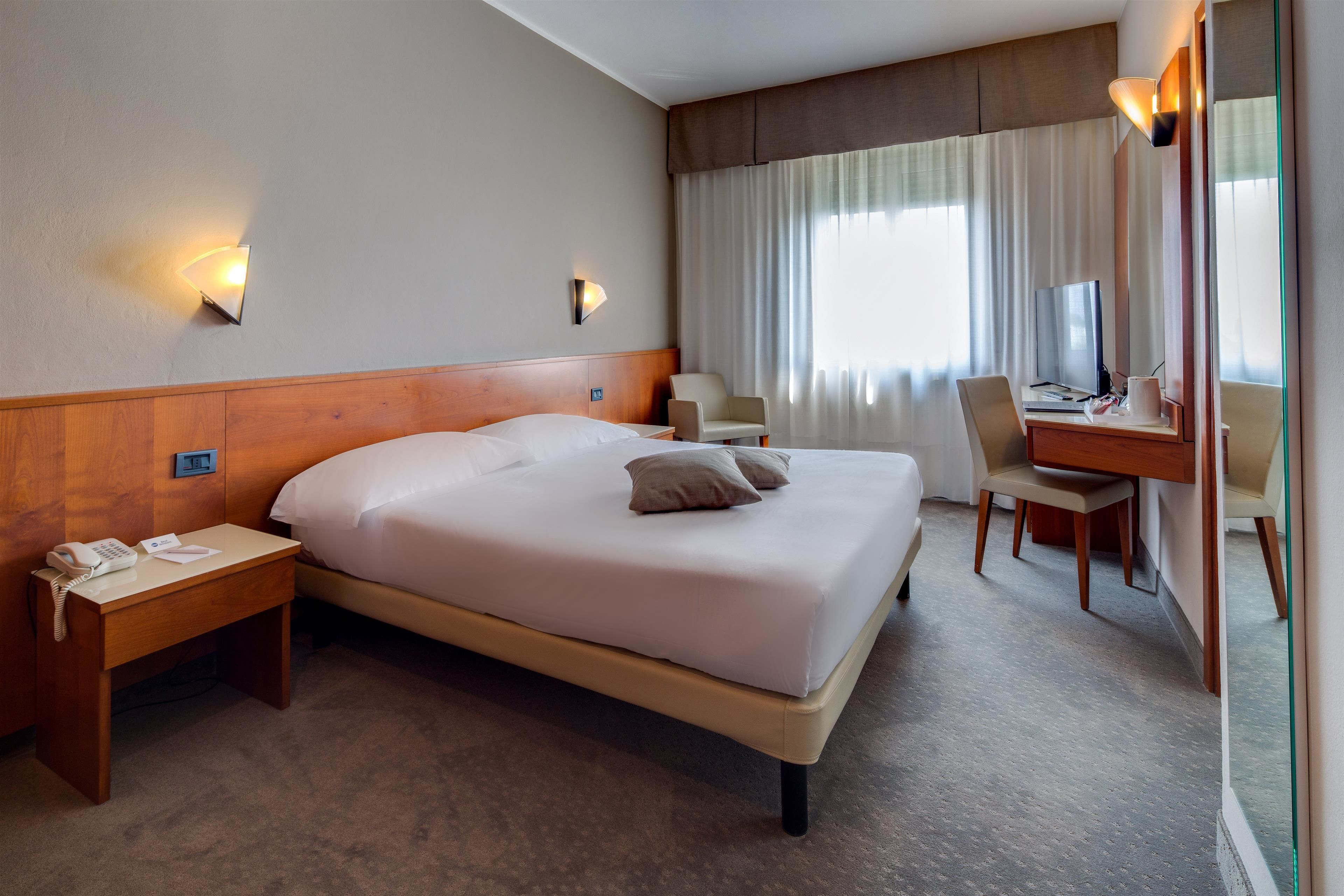 Ein Hotelzimmer mit einem großen Bett, Nachttischen, einem Schreibtisch mit Stuhl und einem Spiegel.