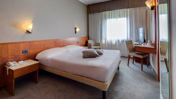 Ein Hotelzimmer mit einem großen Bett, Nachttischen, einem Schreibtisch mit Stuhl und einem Spiegel.