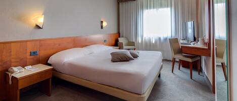 A hotel room with a large bed, bedside tables, a desk with a chair, and a mirror.