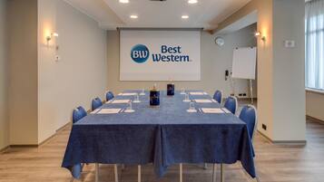 Un salón de conferencias con una larga mesa, sillas, un proyector y una pantalla que muestra la marca Best Western.