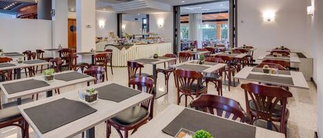 A spacious restaurant with multiple tables and chairs, a buffet area, and large windows offering a view.