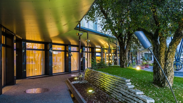 A modern building with large windows, a stone bench, and a tree in the foreground. - Best Western Hotel Turismo (San Martino Buon Albergo)