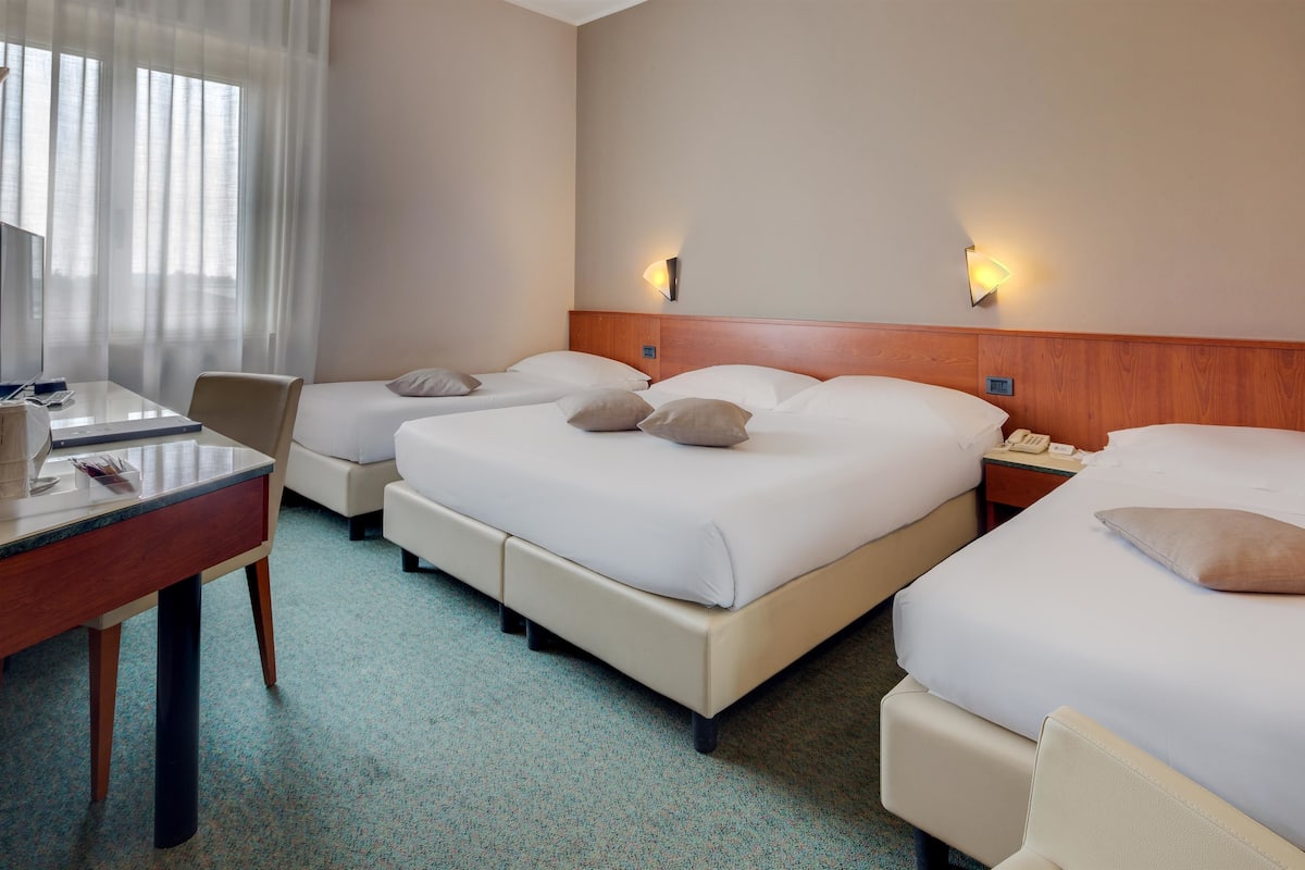 A hotel room with three beds, a desk, a chair, and a telephone.