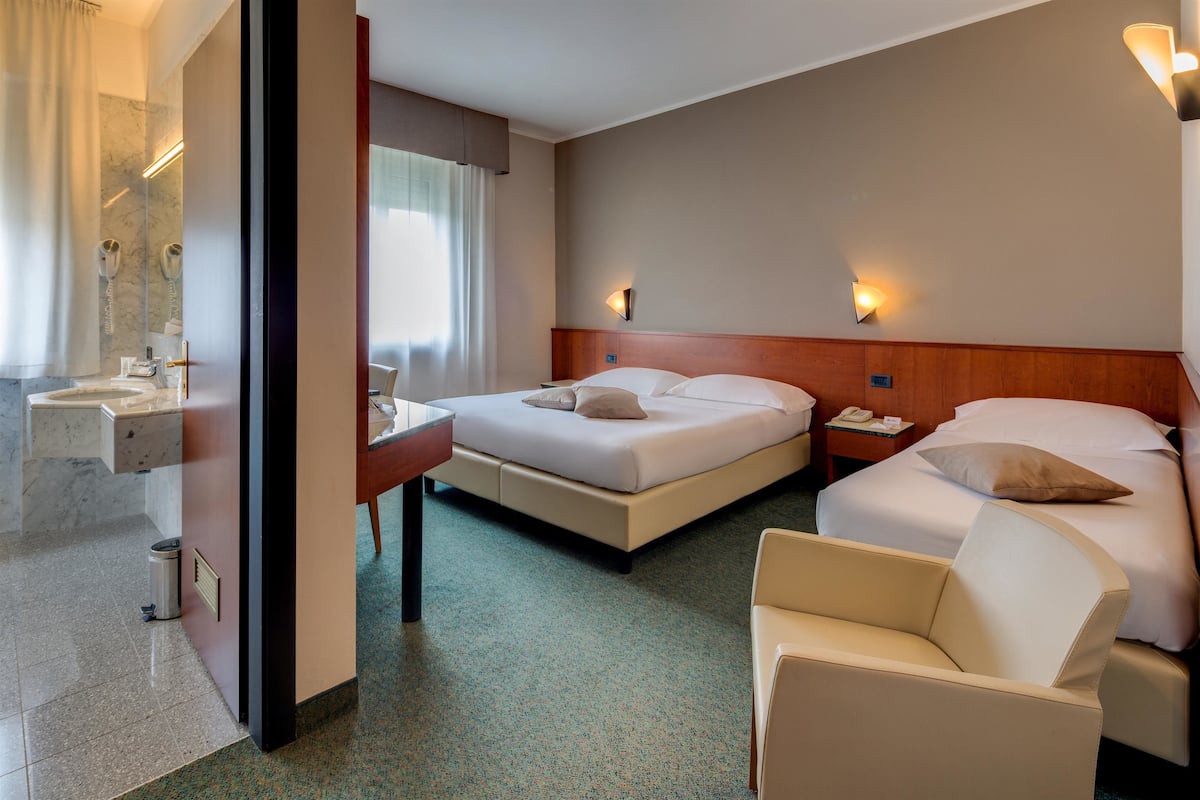A hotel room with two beds, a sitting area, a bathroom with a mirror, and a small table.