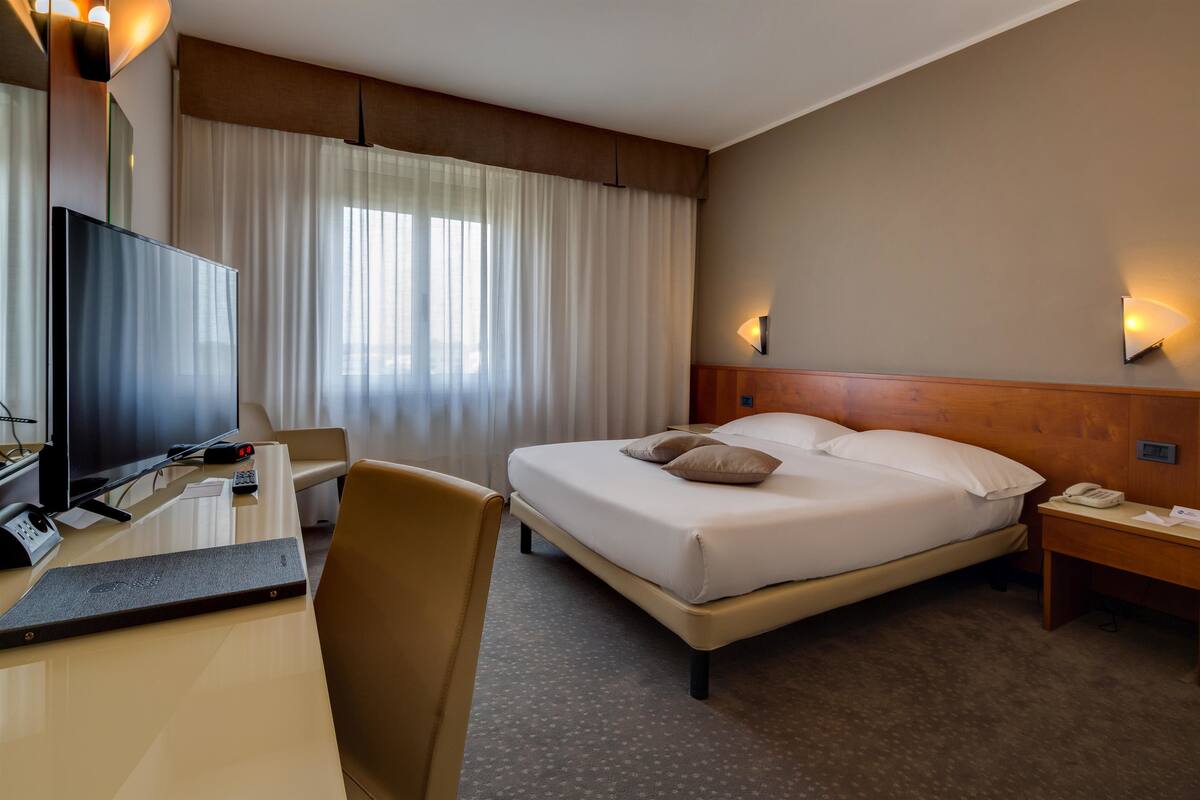 A hotel room with a bed, a desk with a computer, a TV, and a phone.