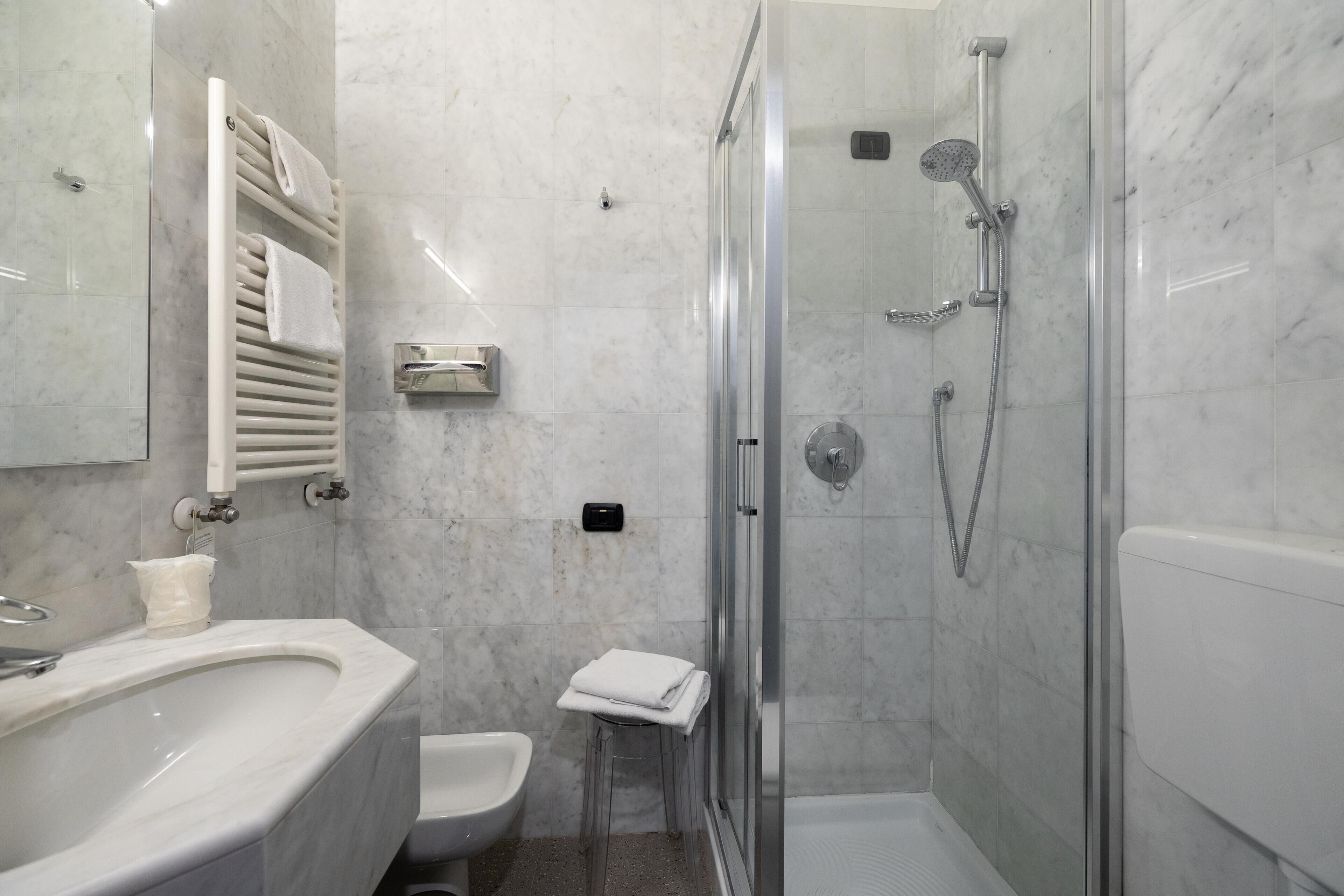 Un baño con lavamanos de mármol, inodoro, ducha con cerramiento de vidrio y perchero para toallas.