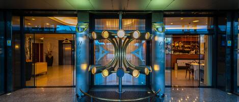 A lobby with a central decorative structure, glass doors leading to a bar area, and a reception desk.
