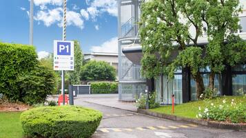 A parking sign labeled P1 with multilingual instructions, a modern building with a cylindrical structure, and well-maintained greenery.