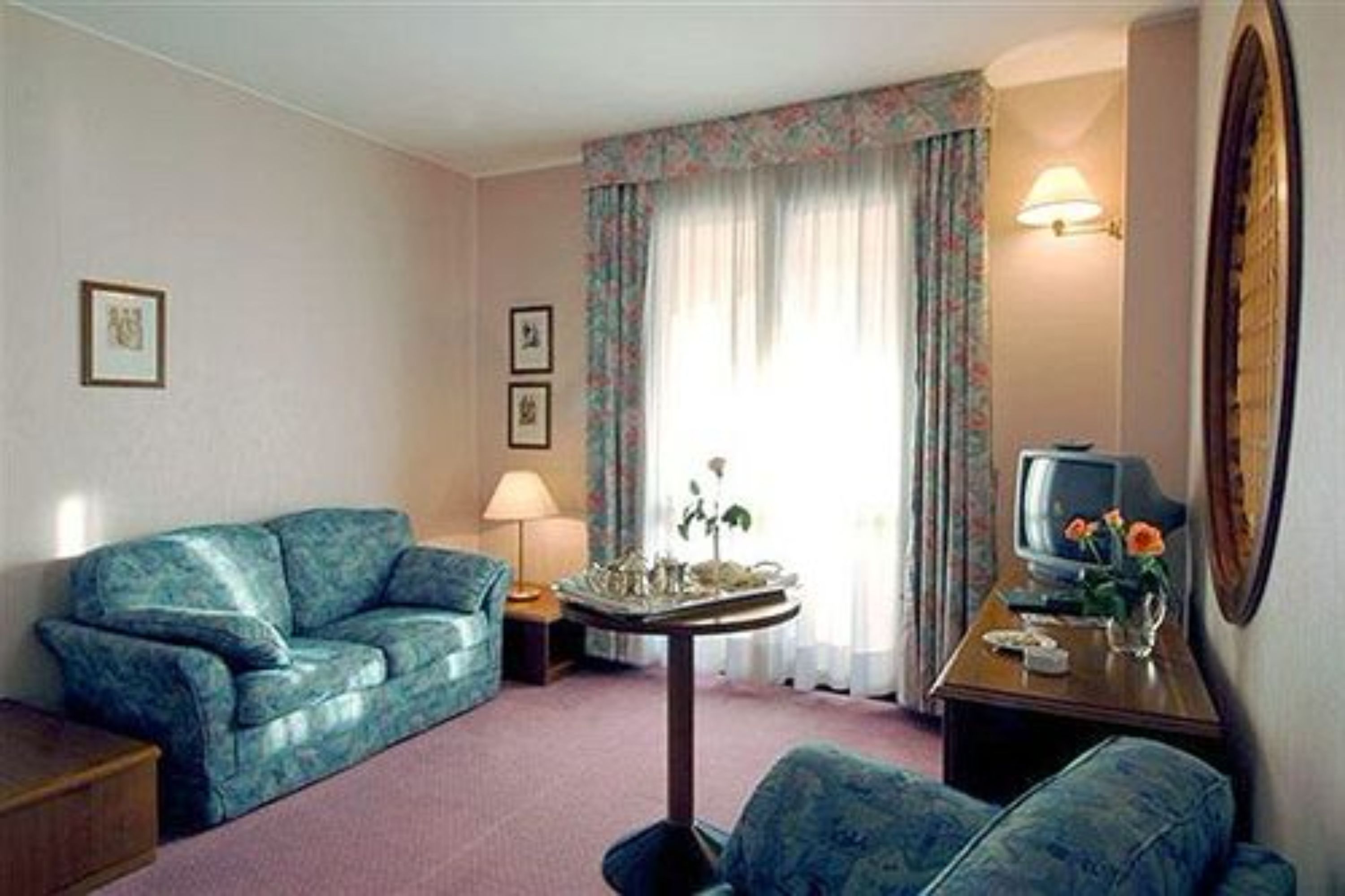 Ein Zimmer mit einem blauen Sofa, einem kleinen Tisch mit Lampe, einem Fernseher und einem dekorativen Gegenstand auf dem Tisch.