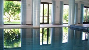 A large indoor swimming pool with clear reflections, surrounded by columns and large windows offering views of greenery outside. - Hotel Martino (Maratea)