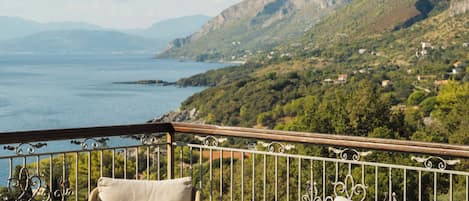 A terrace with wicker furniture, a table, and a view of the sea and mountains.