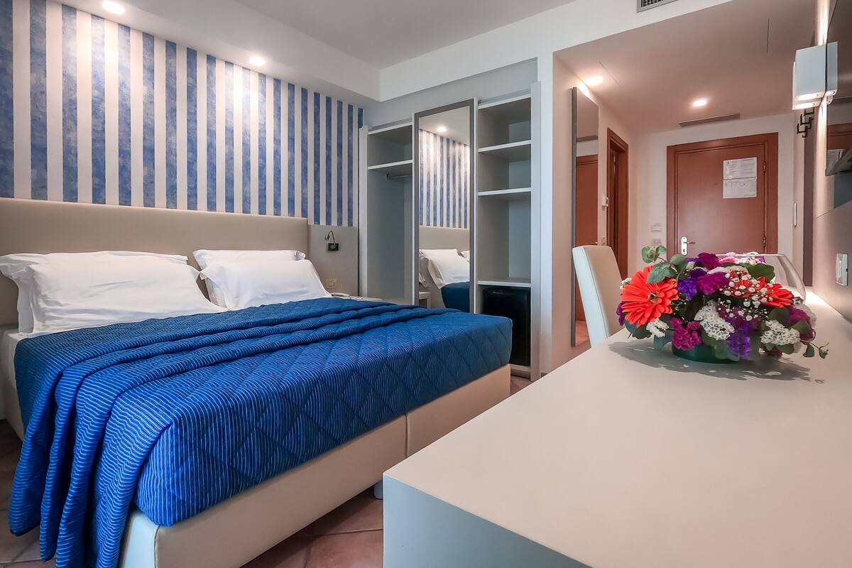 Habitación de hotel con cama, escritorio, silla, armario y baño.