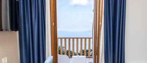 A room with a balcony, a white desk, a blue chair, and a bed.