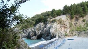 A beach with rocky cliffs, a row of umbrellas, and a tent. - Hotel Martino (Maratea)