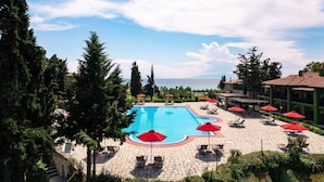Une piscine bordée de parasols rouges, de chaises longues et d’une terrasse en pierre.
