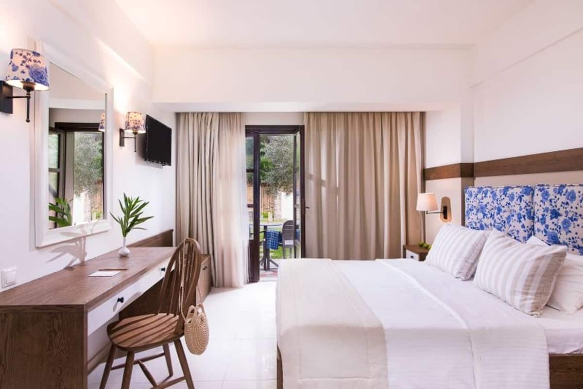 Ein Hotelzimmer mit Bett, Schreibtisch, Stuhl, Fernseher und einem Balkon mit Vorhängen.