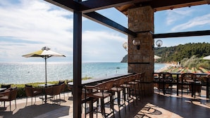 Un espace extérieur aménagé avec des tables et des chaises, offrant une vue panoramique sur la mer et un paysage vallonné.