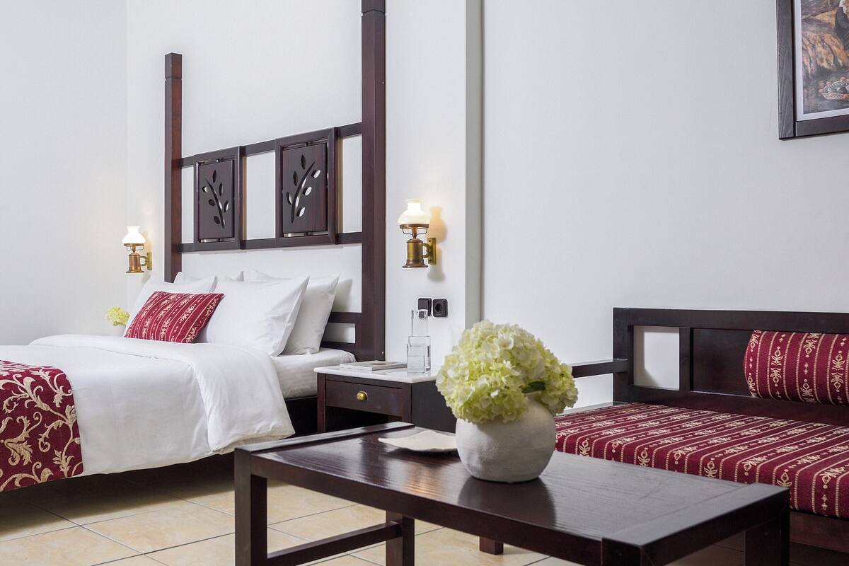 Ein Hotelzimmer mit einem Bett, einem Schlafsofa, einem Nachttisch, einem Tisch und einer Vase mit Blumen.