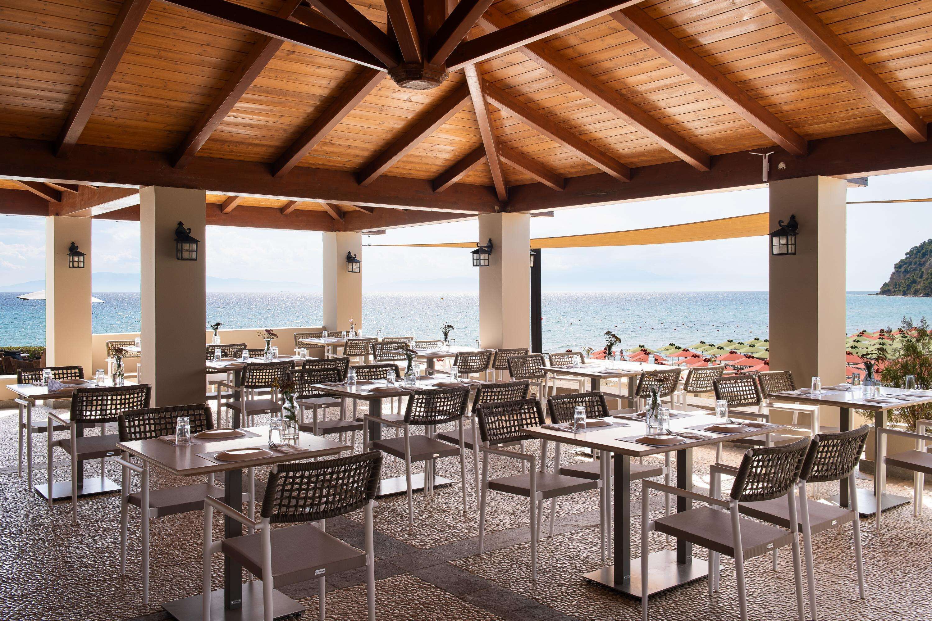 Un espace de restauration en plein air, avec des tables et des chaises, des poutres en bois et une vue sur la mer.