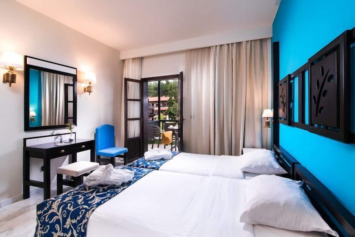 Ein Hotelzimmer mit zwei Betten, einem Schreibtisch, einem Stuhl und Blick ins Freie.
