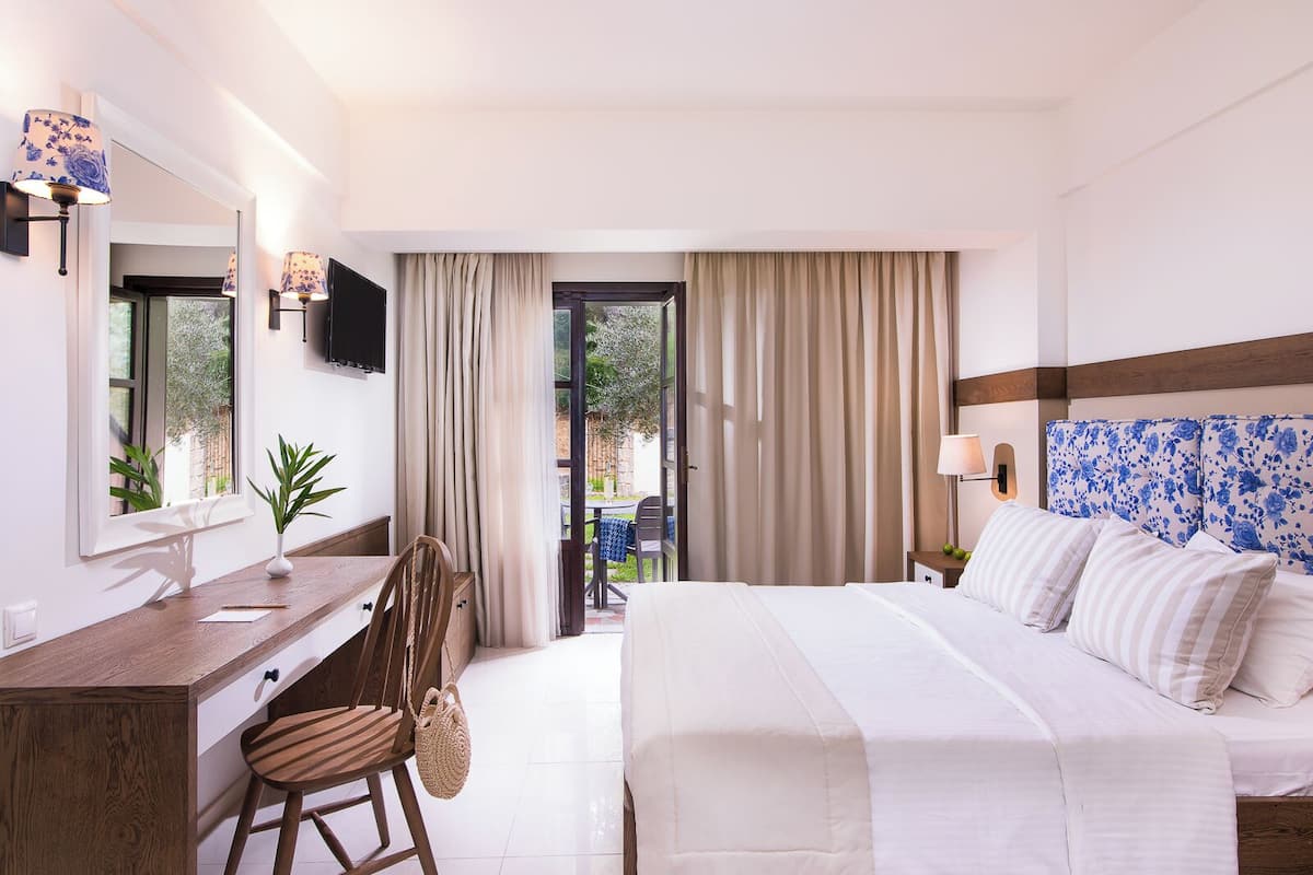 Ein Hotelzimmer mit Bett, Schreibtisch, Stuhl, Fernseher und Blick ins Freie.