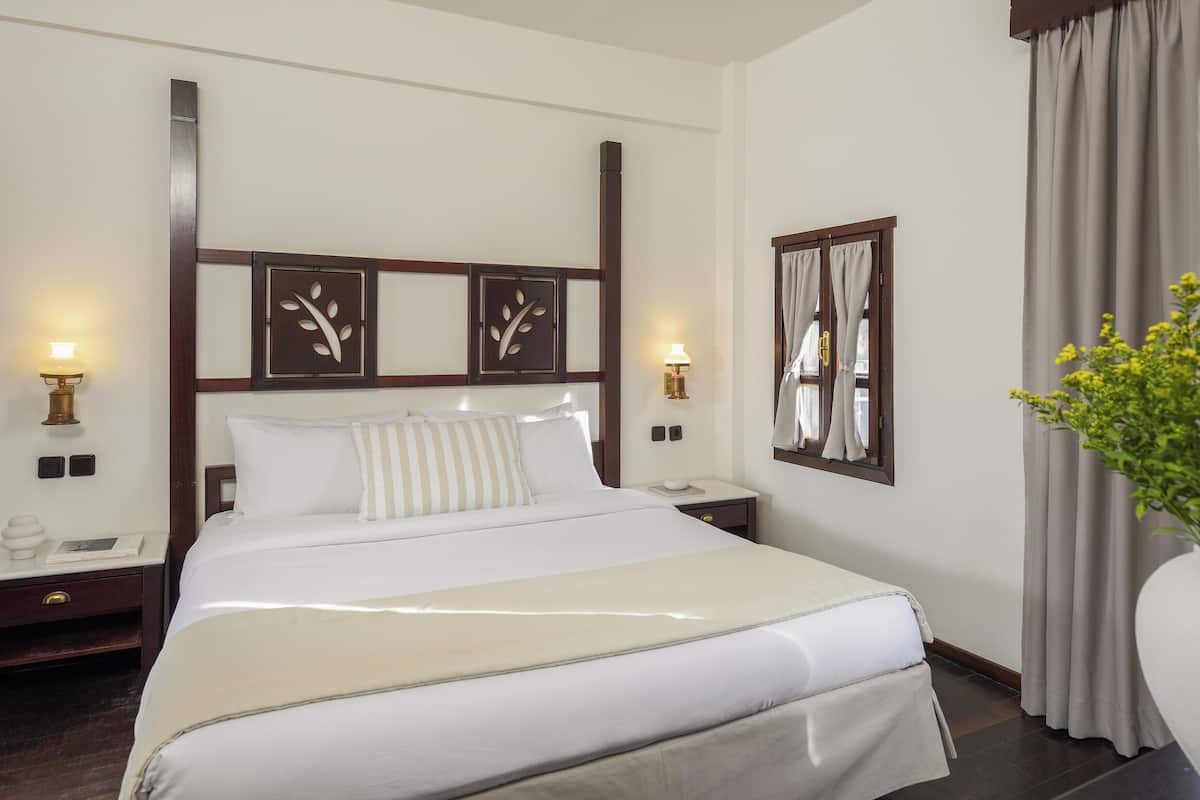 Ein Hotelzimmer mit einem großen Bett, zwei Nachttischen, einem Spiegel und einem Fenster mit Vorhängen.