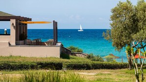 Une vue sur la côte, avec un voilier blanc sur la mer, un espace extérieur aménagé avec des meubles de jardin et un bâtiment doté d’une pergola.