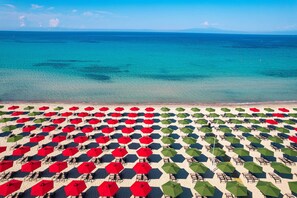 Una playa con hileras de sombrillas y sillas, una vista despejada del océano y una cadena montañosa distante.
