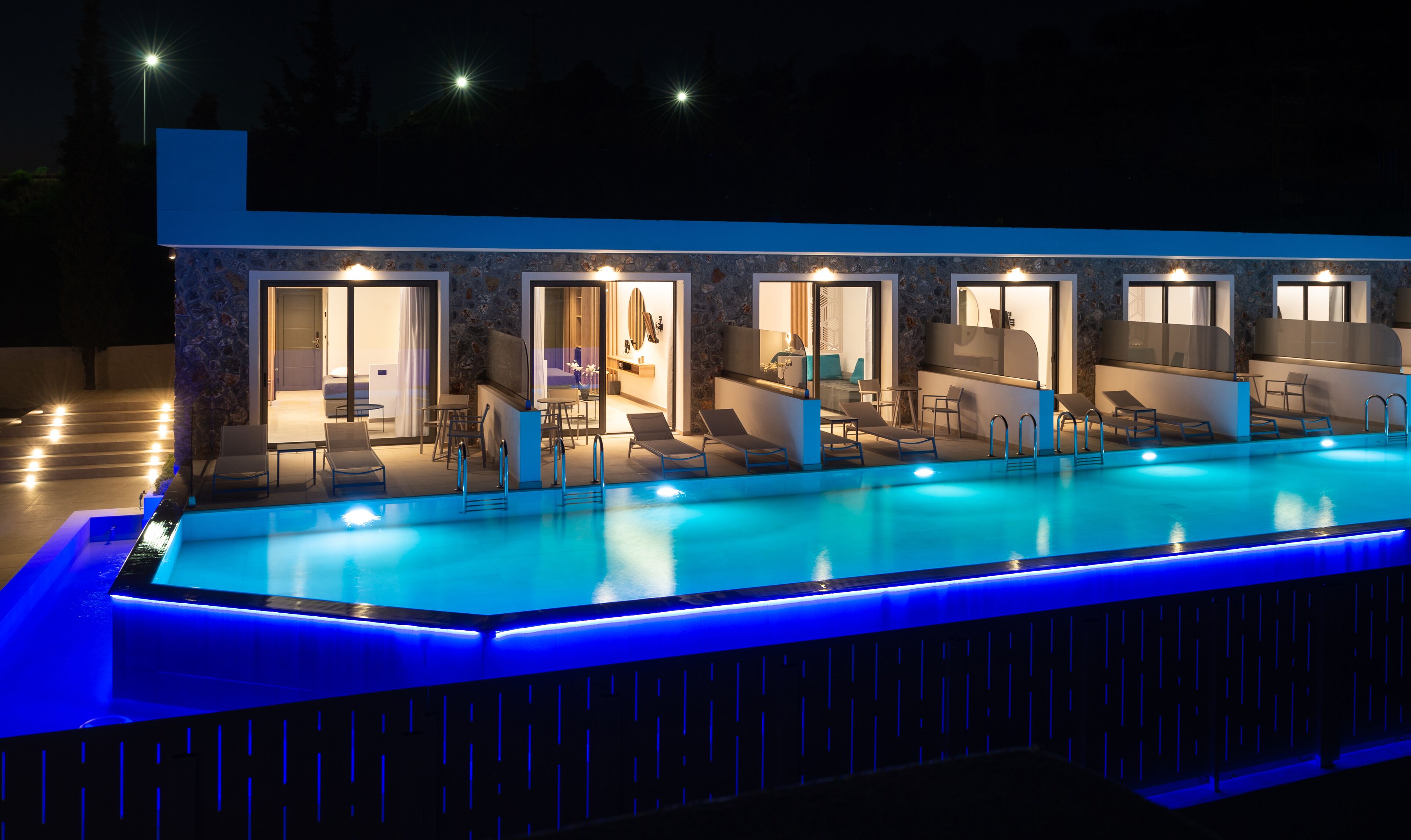 A modern hotel with a swimming pool, outdoor seating, and a stone facade.