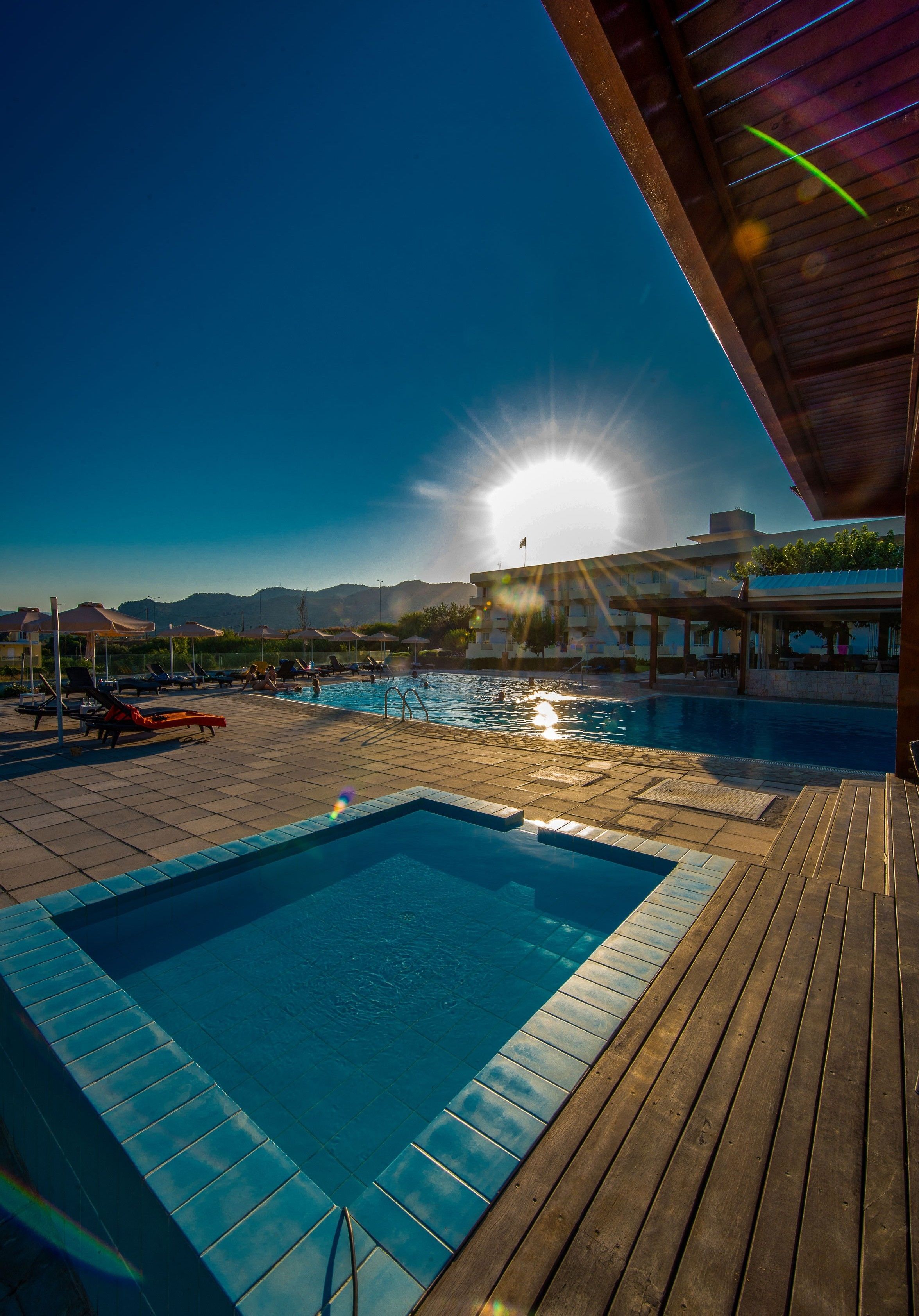 A pool area with a wooden deck, a clear sky, and mountains in the background.