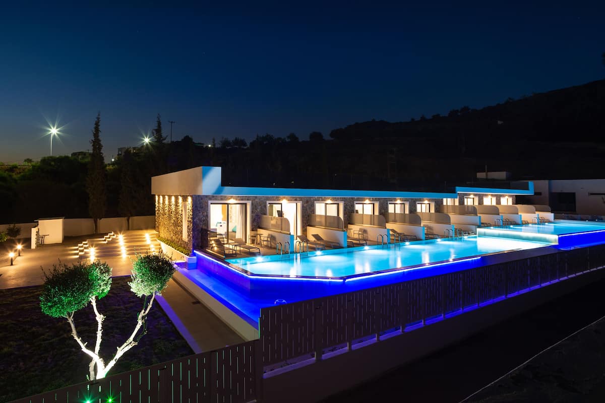 A modern hotel with a swimming pool, outdoor seating, and a well-lit entrance.