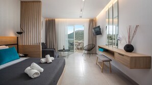 A modern hotel room with a bed, a desk, a chair, a TV, and a balcony with a view. - Zoes Hotel (Rhodes)