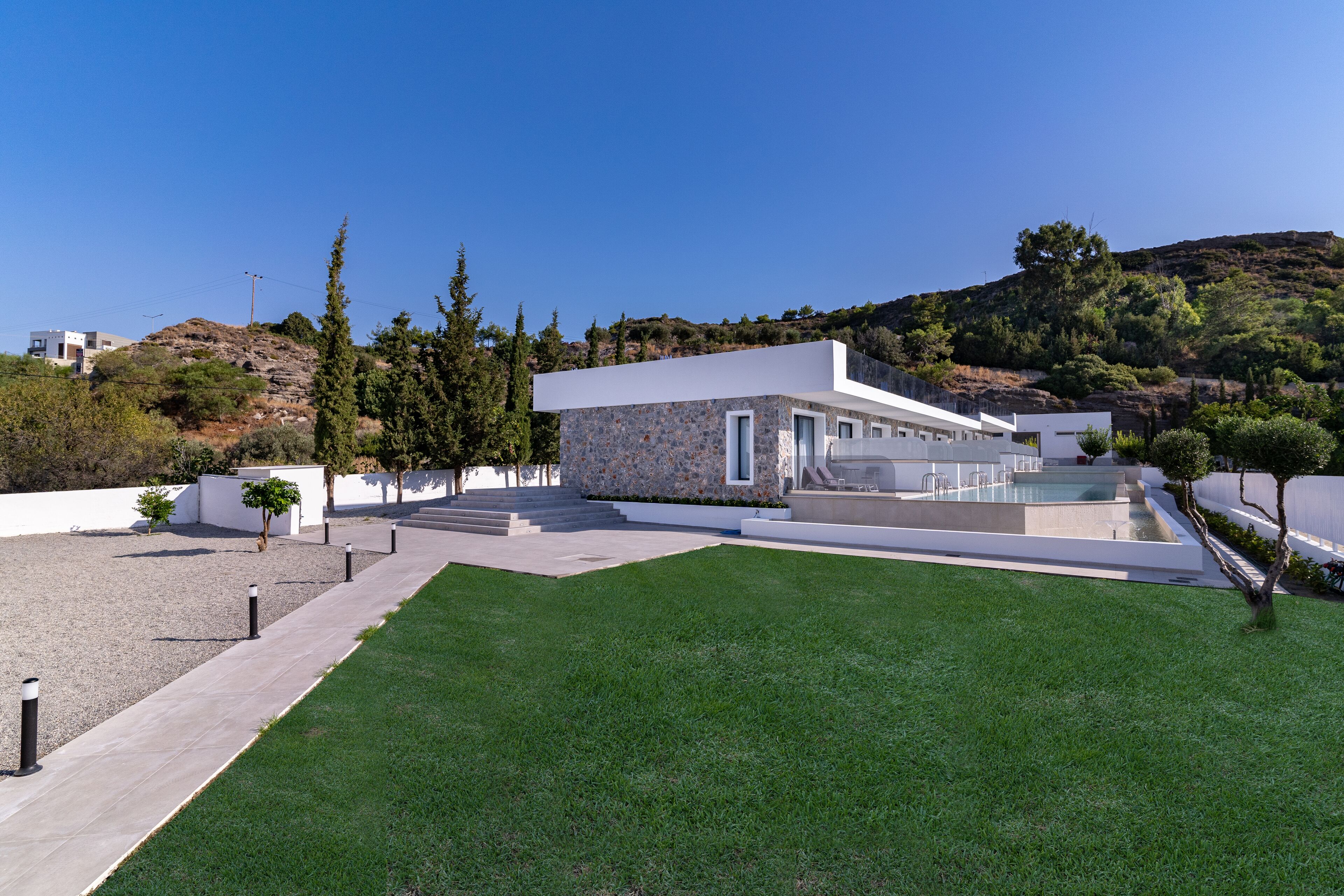 A modern house with a swimming pool, a well-maintained lawn, and a view of a hilly landscape.