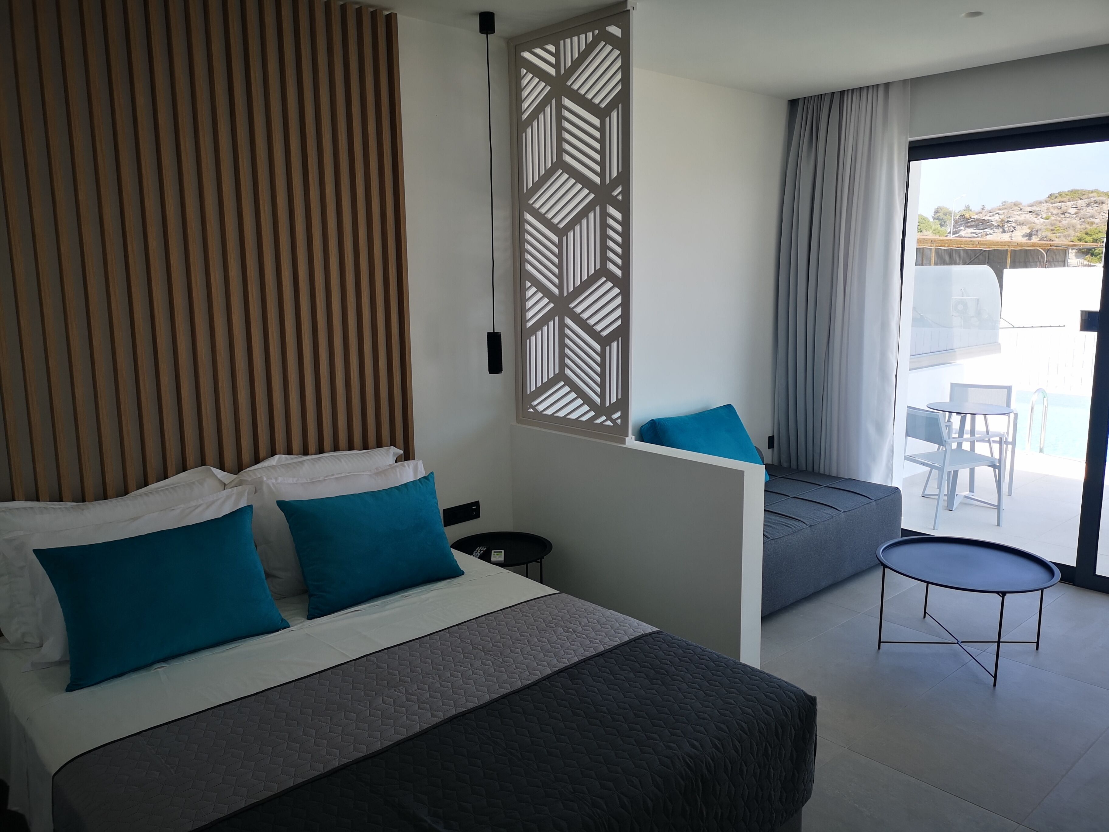 Una habitación de hotel moderna con una cama grande, una mesita y un balcón con vistas.