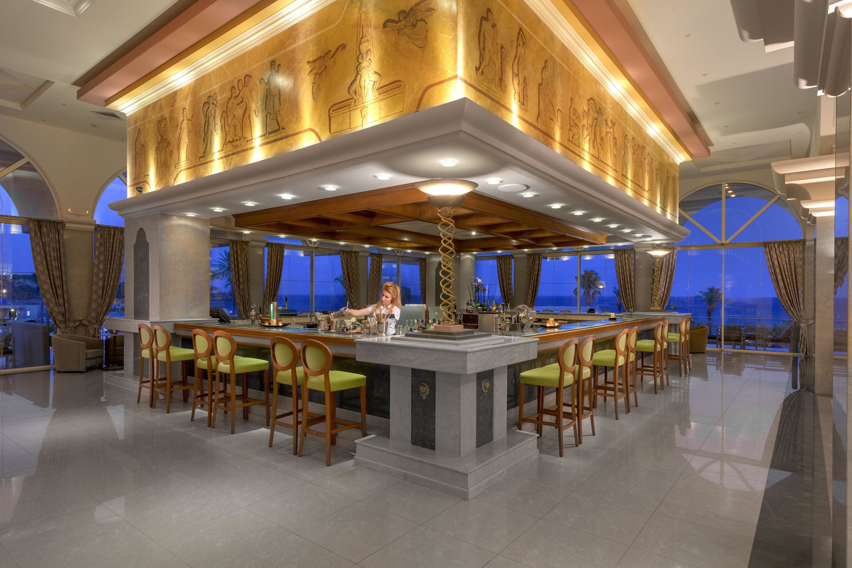 A bar area with a central island, multiple bar stools, and a view of the outside.