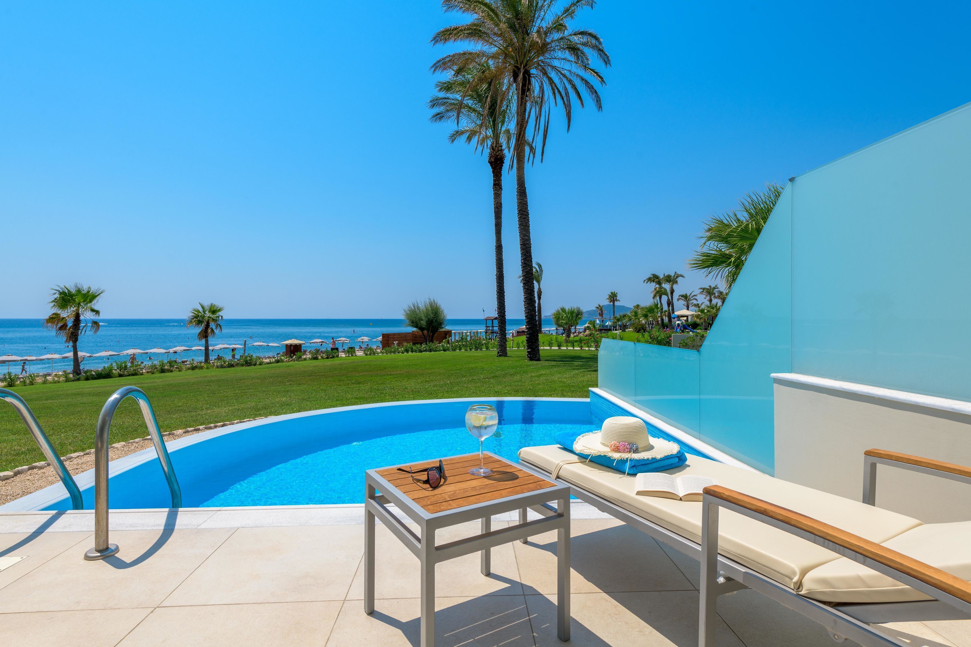 A poolside area with a view of the ocean, a lounge chair, and a table with a glass and sunglasses.