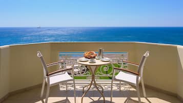 A balcony with a table set for two, overlooking a clear blue sea with a sailboat in the distance.