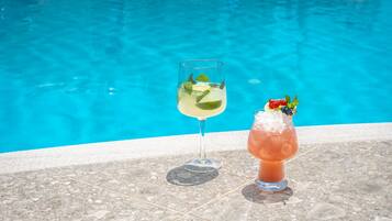 Dos bebidas sobre una superficie de baldosas junto a una piscina.