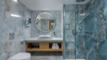 Un baño moderno con lavamanos de mármol, un espejo redondo, cabina de ducha con mampara de vidrio y un inodoro.