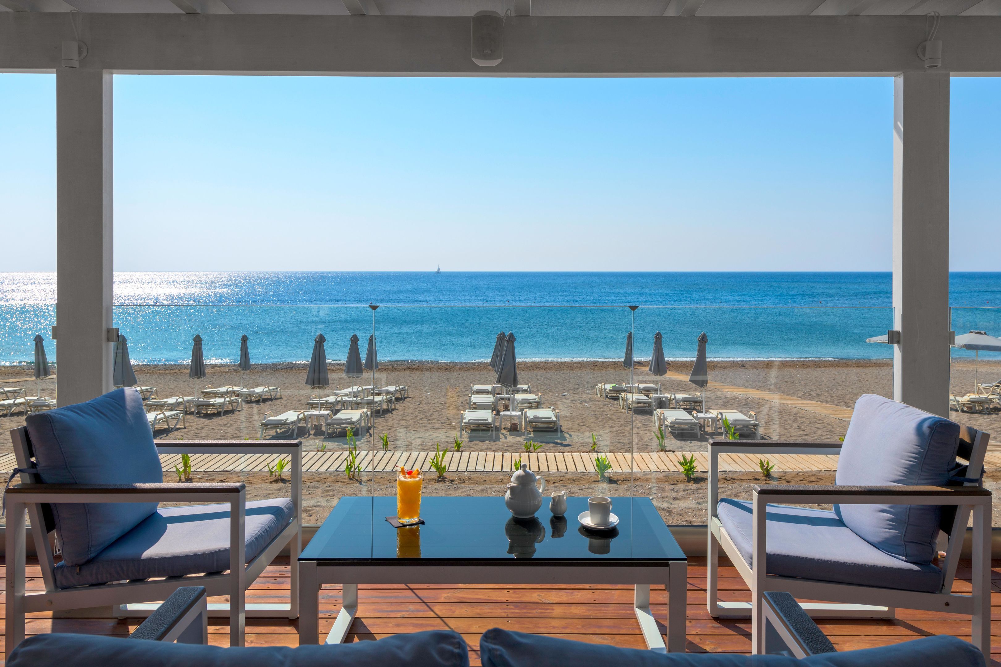 Une terrasse avec vue sur la plage et l’océan. On y trouve des chaises longues et une table avec une boisson et une théière.