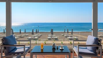 Une terrasse avec vue sur la plage et l’océan. On y trouve des chaises longues et une table avec une boisson et une théière.