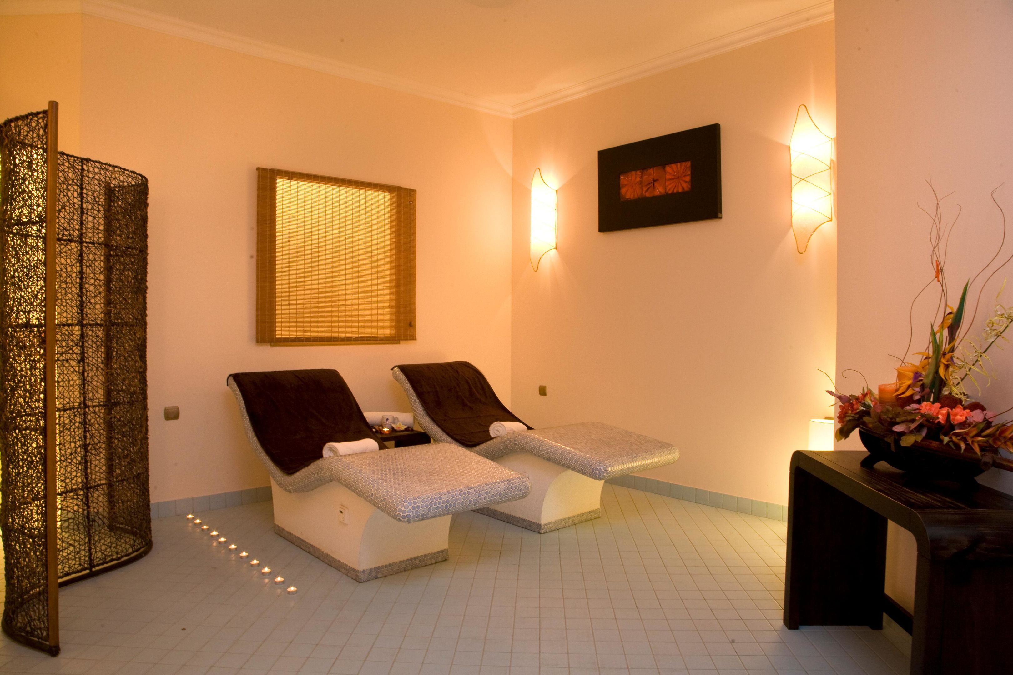 A spa room with two reclining chairs, a decorative screen, a wall-mounted light fixture, and a framed artwork.